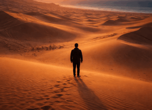 شخص وحيد يقف وسط صحراء شاسعة عند الغروب بين تلاقي الرمال والبحر في مشهد يعكس العزلة والتأمل.